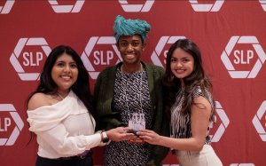 Three people holding an award smiling in front of a red backdrop.